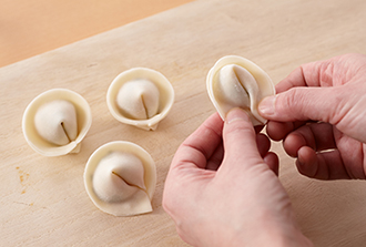 餃子の皮の真ん中にたねをのせ、端に水（分量外）を塗る。半分に折りたたみ、両端を引き寄せ、水をつけてしっかり指で押さえて止める。